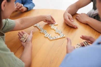 Photo of Friends playing dominoes at wooden table, closeup