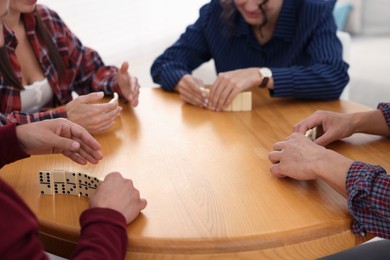 Photo of Friends playing dominoes at wooden table indoors, closeup