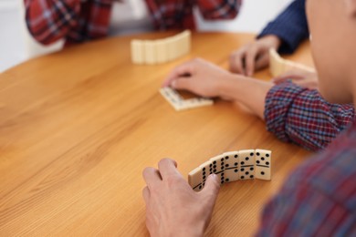 Photo of Friends playing dominoes at wooden table, closeup