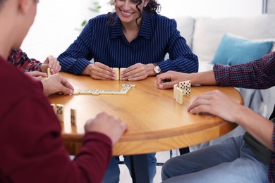Photo of Friends playing dominoes at wooden table indoors, closeup