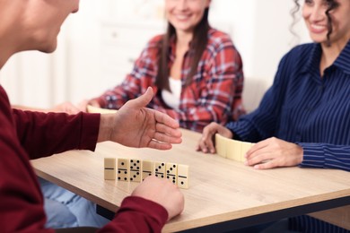 Photo of Friends playing dominoes at light wooden table indoors, closeup