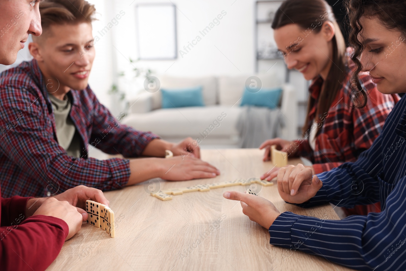Friends playing dominoes at light wooden table indoors Photo of Friends playing dominoes at light wooden table indoors