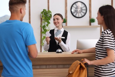 Photo of Smiling receptionist in uniform giving hotel key card to couple of tourists at reception desk indoors