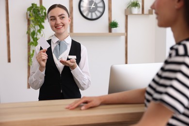 Photo of Smiling receptionist in uniform with hotel key card working with guest at reception desk indoors