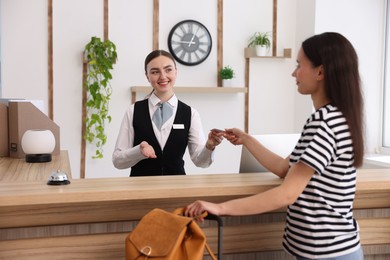 Photo of Smiling receptionist in uniform giving hotel key card to guest at reception desk indoors