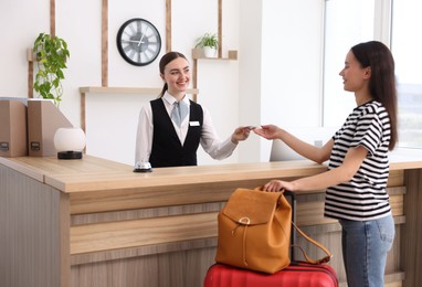 Photo of Smiling receptionist in uniform giving hotel key card to guest at reception desk indoors