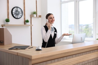 Photo of Smiling receptionist talking with client by phone at reception desk in hotel