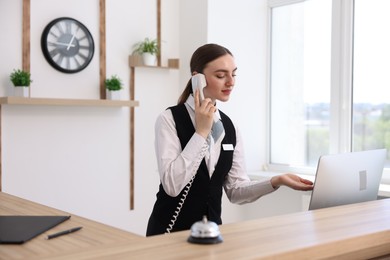 Photo of Receptionist talking with client by phone at reception desk in hotel
