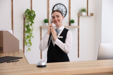Photo of Smiling receptionist talking with client by phone at reception desk in hotel