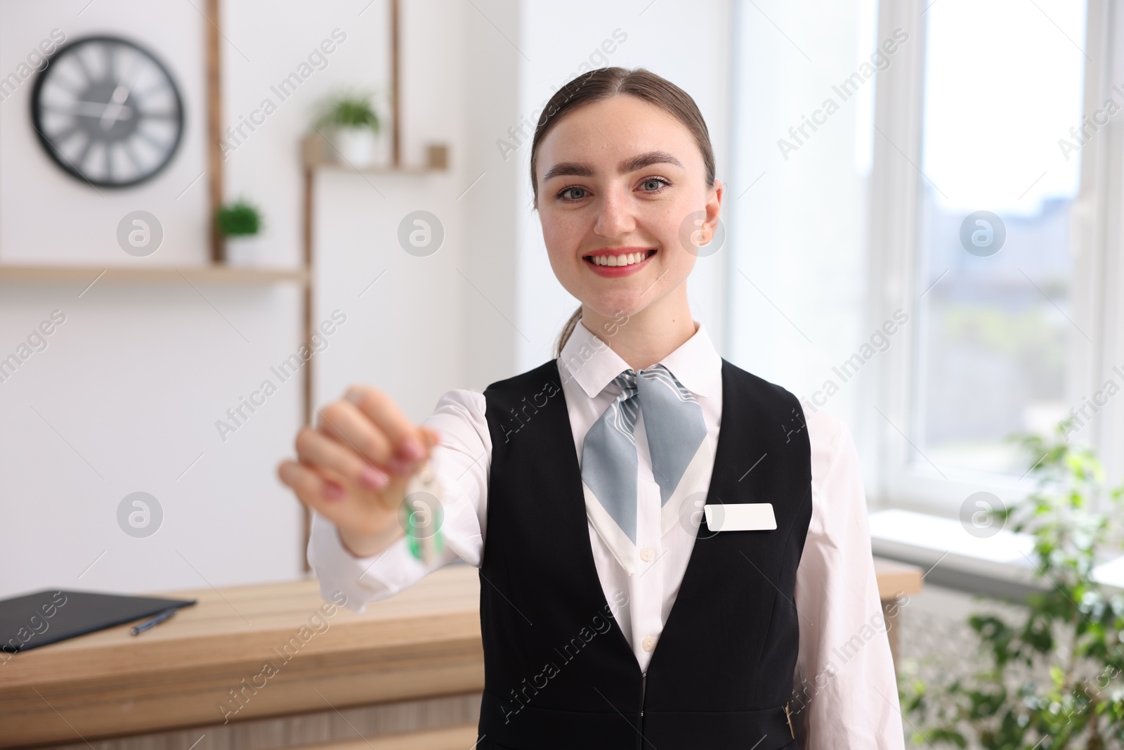 Photo of Portrait of smiling receptionist giving guest room key in hotel