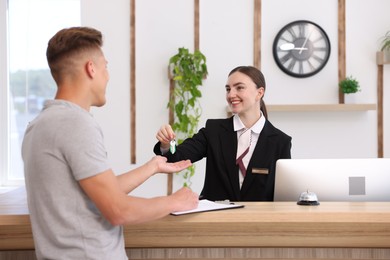 Photo of Smiling receptionist in uniform giving guest room key to client at reception desk in hotel