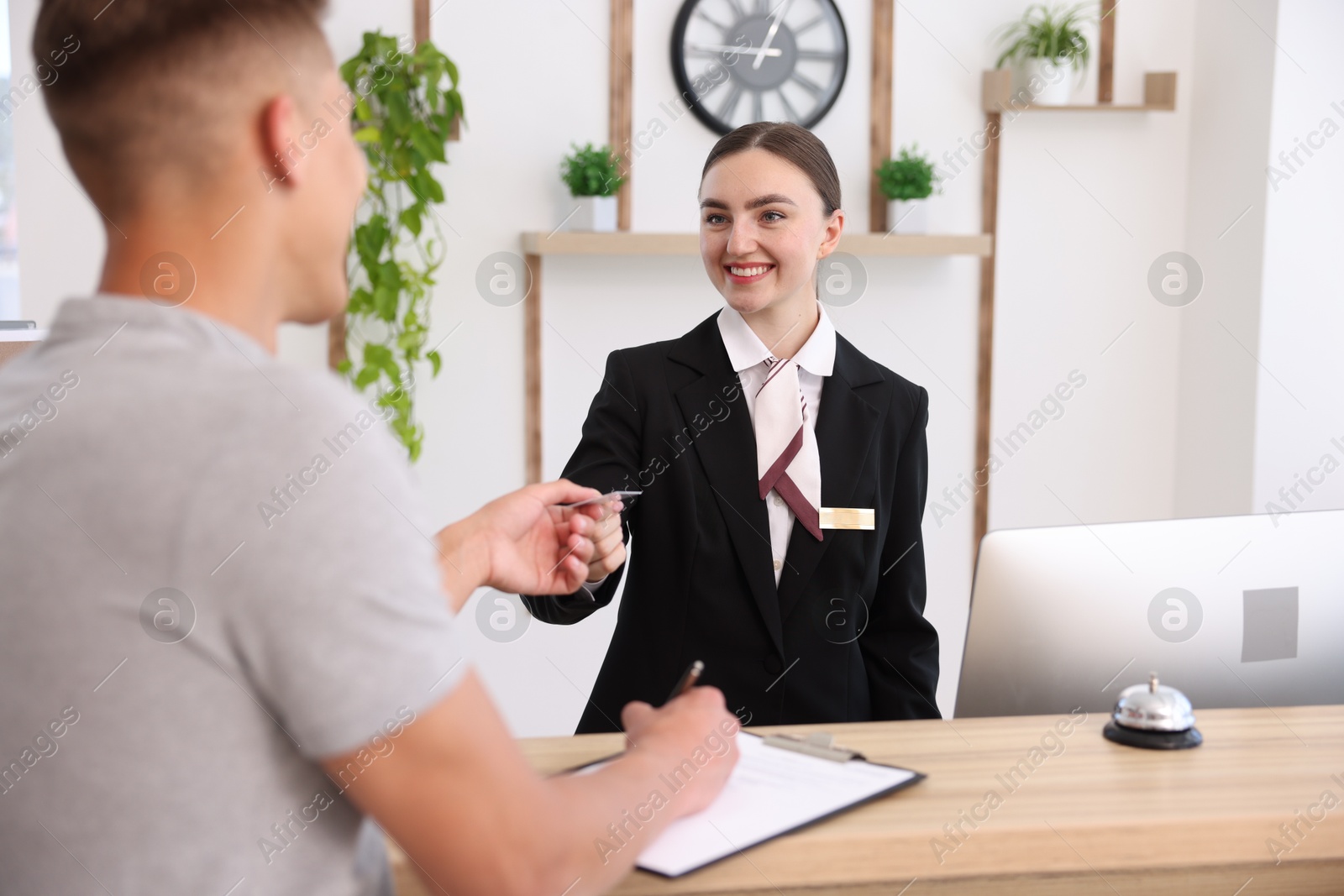 Smiling receptionist in uniform giving hotel key card to guest at reception desk indoors Photo of Smiling receptionist in uniform giving hotel key card to guest at reception desk indoors