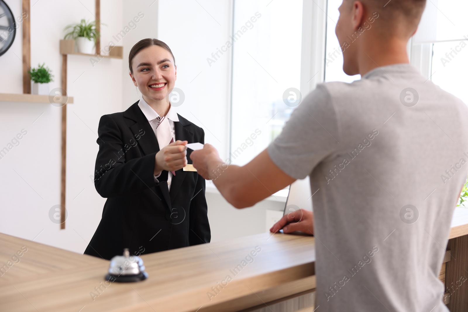 Photo of Smiling receptionist in uniform giving hotel key card to guest at reception desk indoors