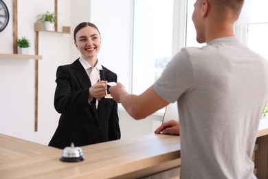 Photo of Smiling receptionist in uniform giving hotel key card to guest at reception desk indoors