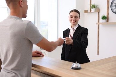 Photo of Smiling receptionist in uniform giving hotel key card to guest at reception desk indoors