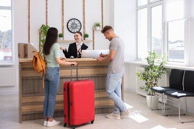 Photo of Smiling receptionist working with clients at reception desk in hotel