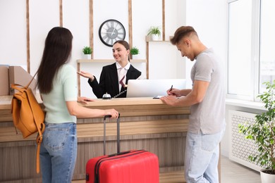 Photo of Smiling receptionist working with clients at reception desk in hotel