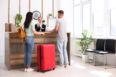 Photo of Smiling receptionist working with clients at reception desk in hotel