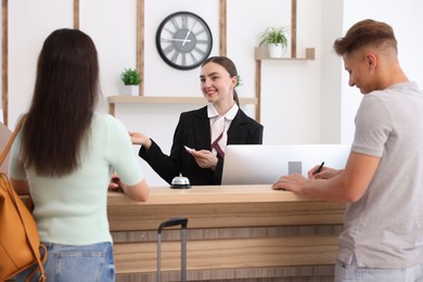 Photo of Smiling receptionist in uniform with hotel key card working with clients at reception desk indoors