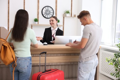 Photo of Smiling receptionist in uniform with hotel key card working with clients at reception desk indoors