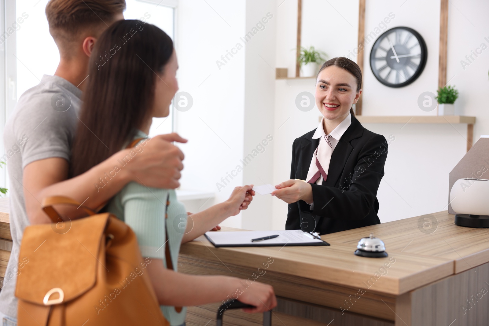 Smiling receptionist in uniform giving hotel key card to couple of tourists at reception desk indoors Photo of Smiling receptionist in uniform giving hotel key card to couple of tourists at reception desk indoors