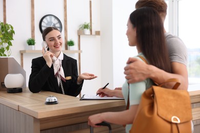 Photo of Smiling receptionist working with clients at reception desk in hotel