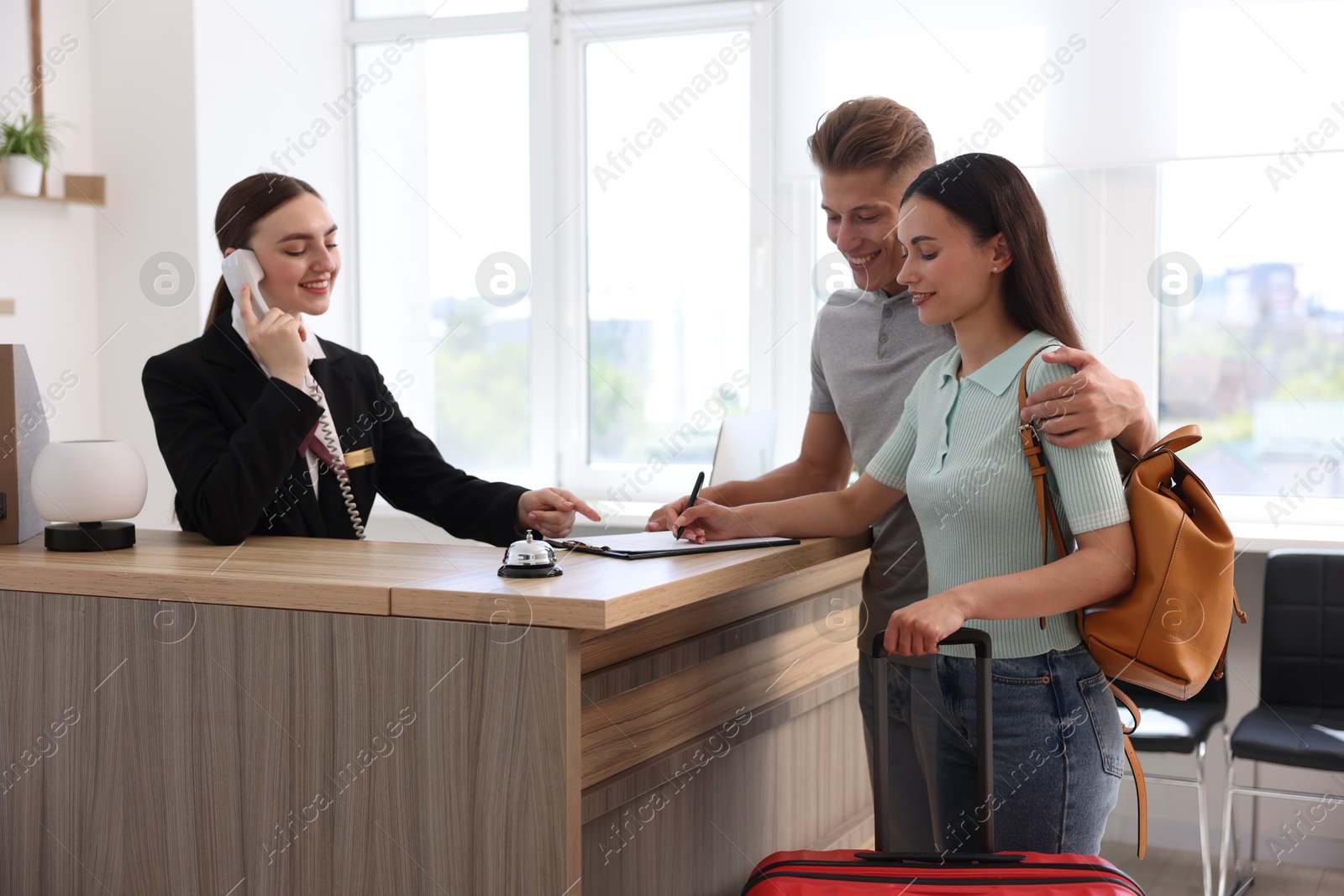 Smiling receptionist working with clients at reception desk in hotel Photo of Smiling receptionist working with clients at reception desk in hotel