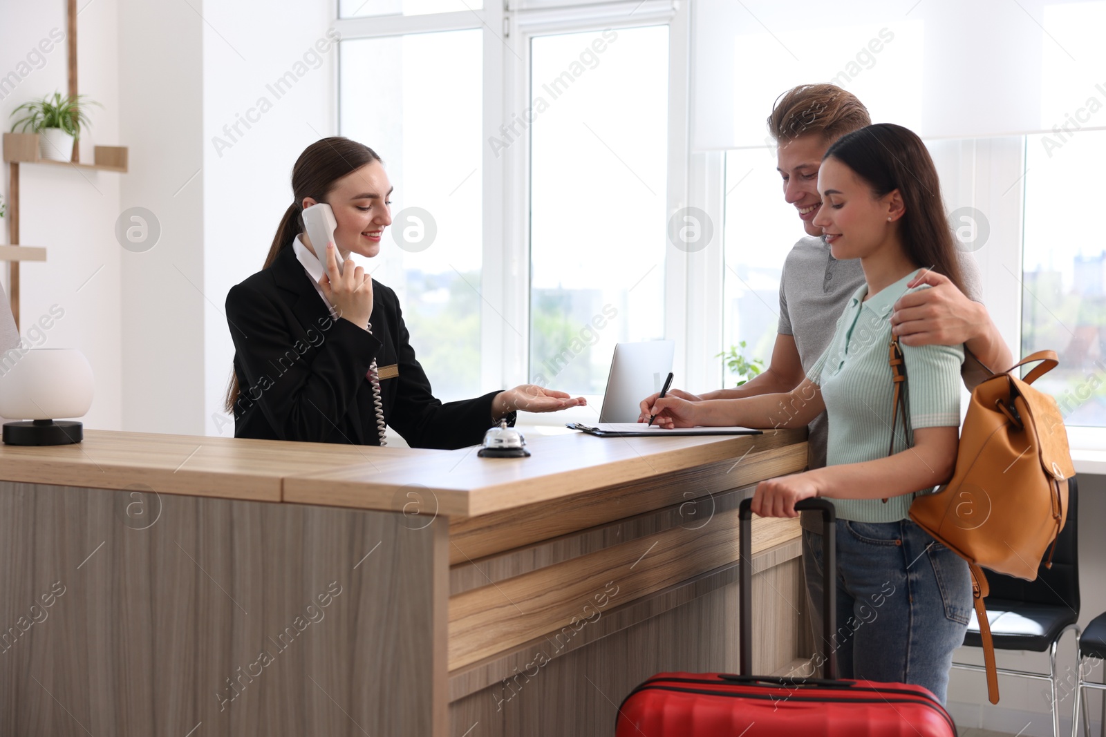 Smiling receptionist working with clients at reception desk in hotel Photo of Smiling receptionist working with clients at reception desk in hotel