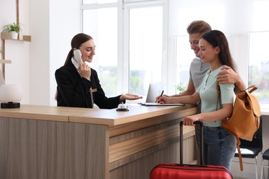 Photo of Smiling receptionist working with clients at reception desk in hotel