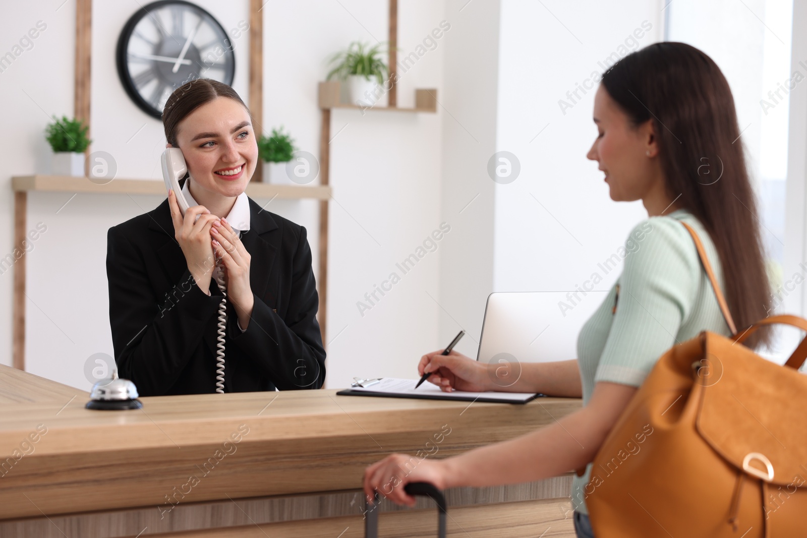 Smiling receptionist working with guest at reception desk indoors Photo of Smiling receptionist working with guest at reception desk indoors