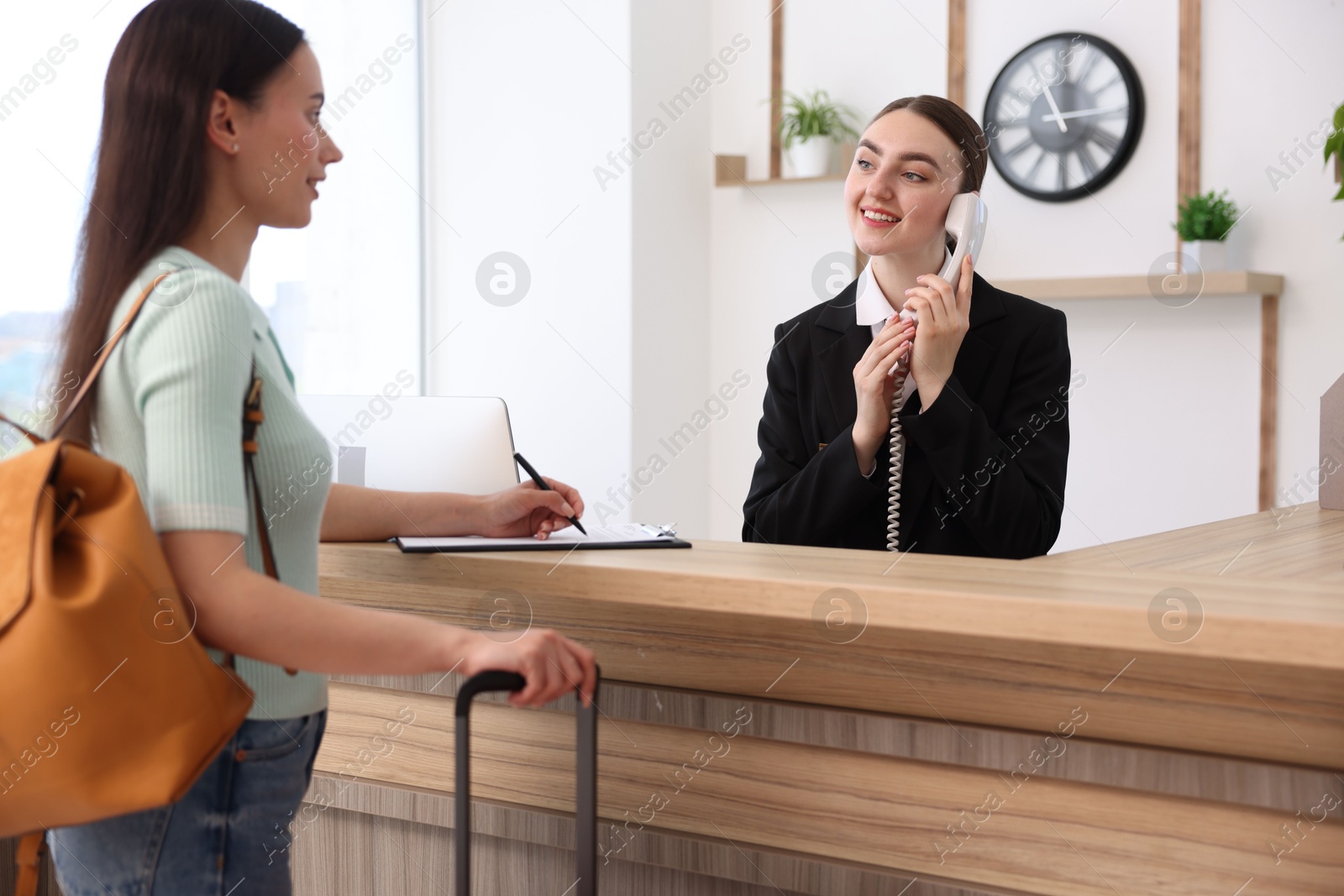 Smiling receptionist working with guest at reception desk indoors Photo of Smiling receptionist working with guest at reception desk indoors