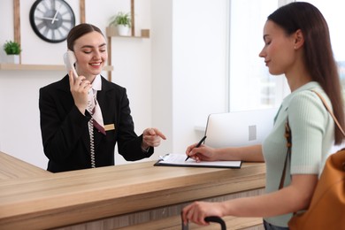 Photo of Smiling receptionist working with guest at reception desk indoors