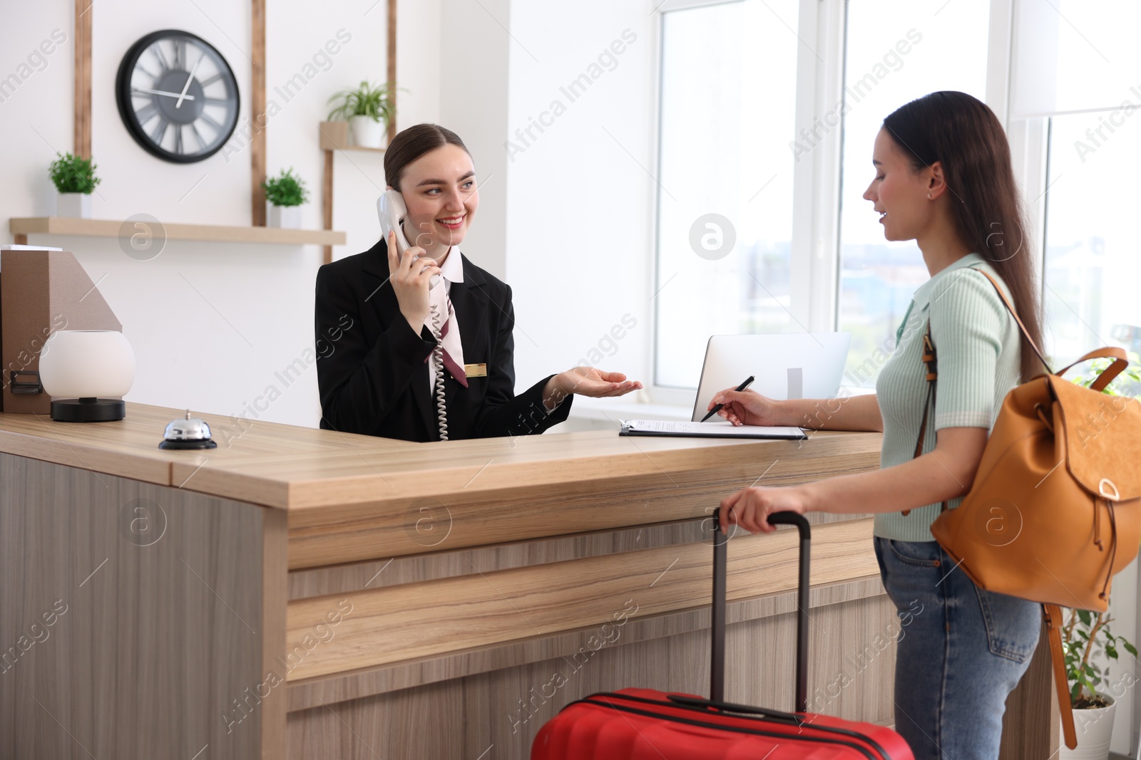 Smiling receptionist working with guest at reception desk indoors Photo of Smiling receptionist working with guest at reception desk indoors