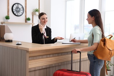 Photo of Smiling receptionist working with guest at reception desk indoors