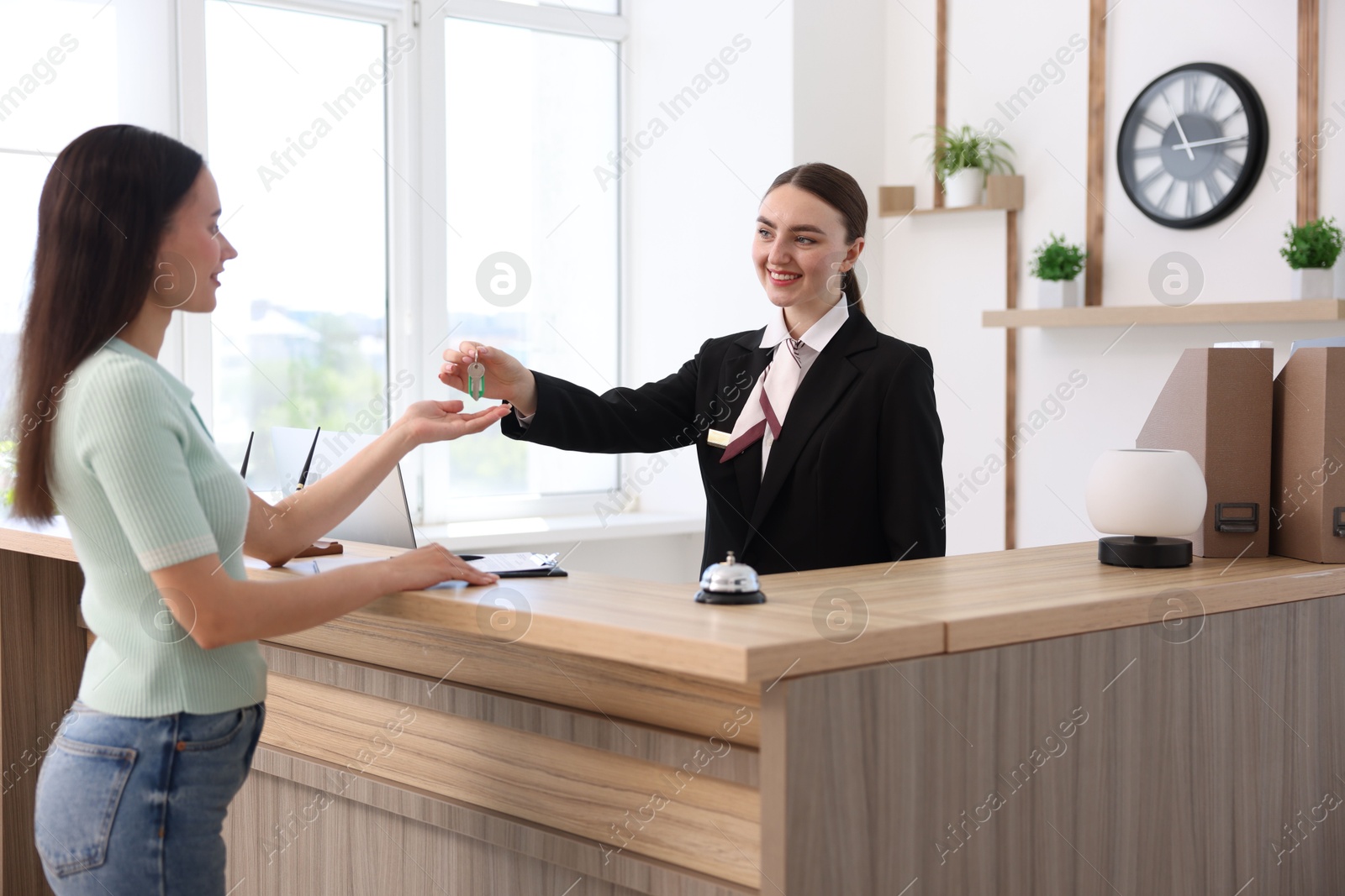 Smiling receptionist in uniform giving guest room key to client at reception desk in hotel Photo of Smiling receptionist in uniform giving guest room key to client at reception desk in hotel