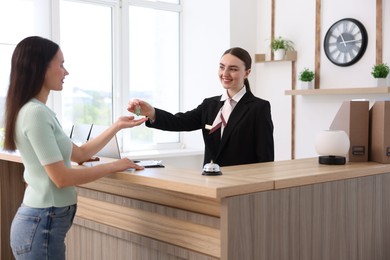 Photo of Smiling receptionist in uniform giving guest room key to client at reception desk in hotel