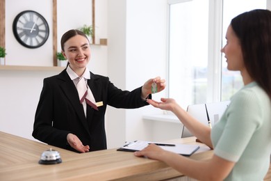 Photo of Smiling receptionist in uniform giving guest room key to client at reception desk in hotel