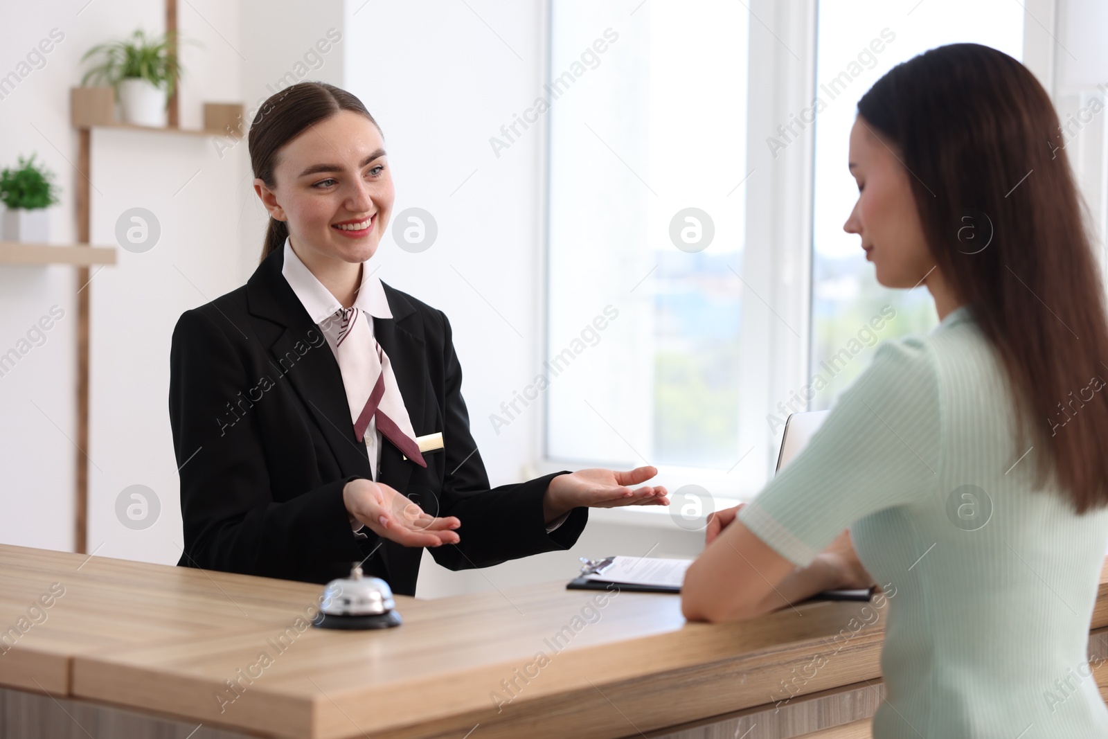 Smiling receptionist working with guest at reception desk indoors Photo of Smiling receptionist working with guest at reception desk indoors