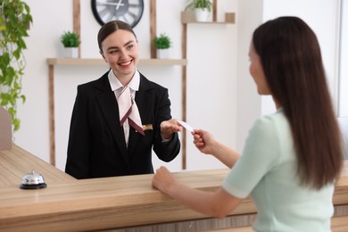 Photo of Smiling receptionist receiving hotel key card from client at reception desk indoors