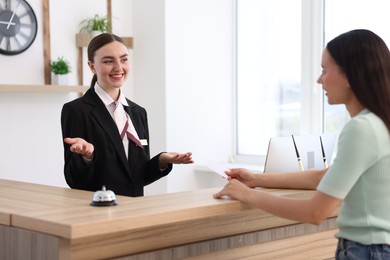 Photo of Smiling receptionist working with guest at reception desk indoors