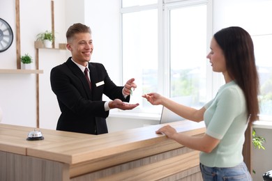 Photo of Smiling receptionist in uniform giving guest room key to client at reception desk in hotel