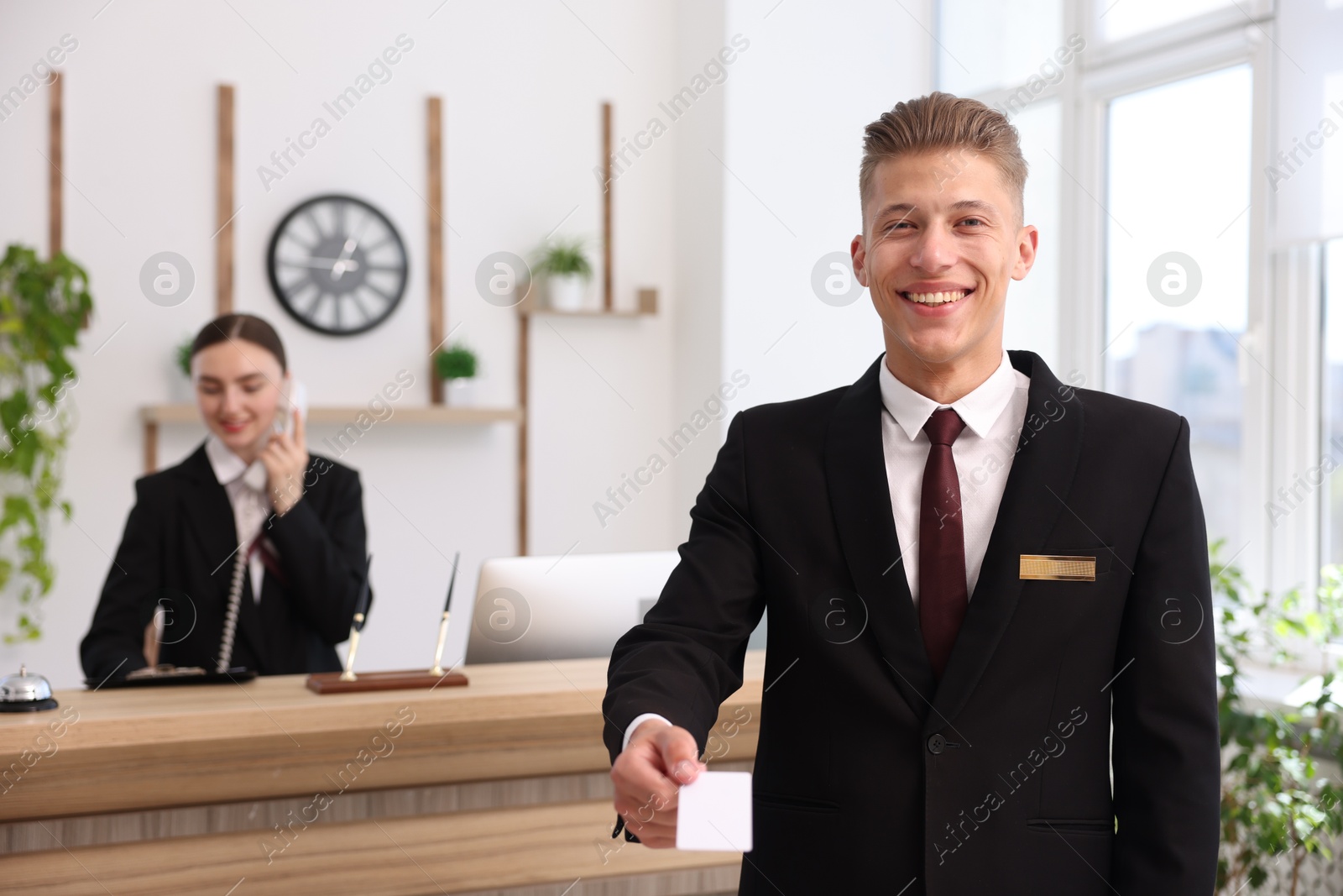 Smiling receptionist in uniform giving key card and his colleague working in hotel, selective focus Photo of Smiling receptionist in uniform giving key card and his colleague working in hotel, selective focus