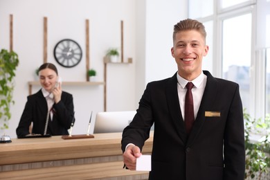 Photo of Smiling receptionist in uniform giving key card and his colleague working in hotel, selective focus