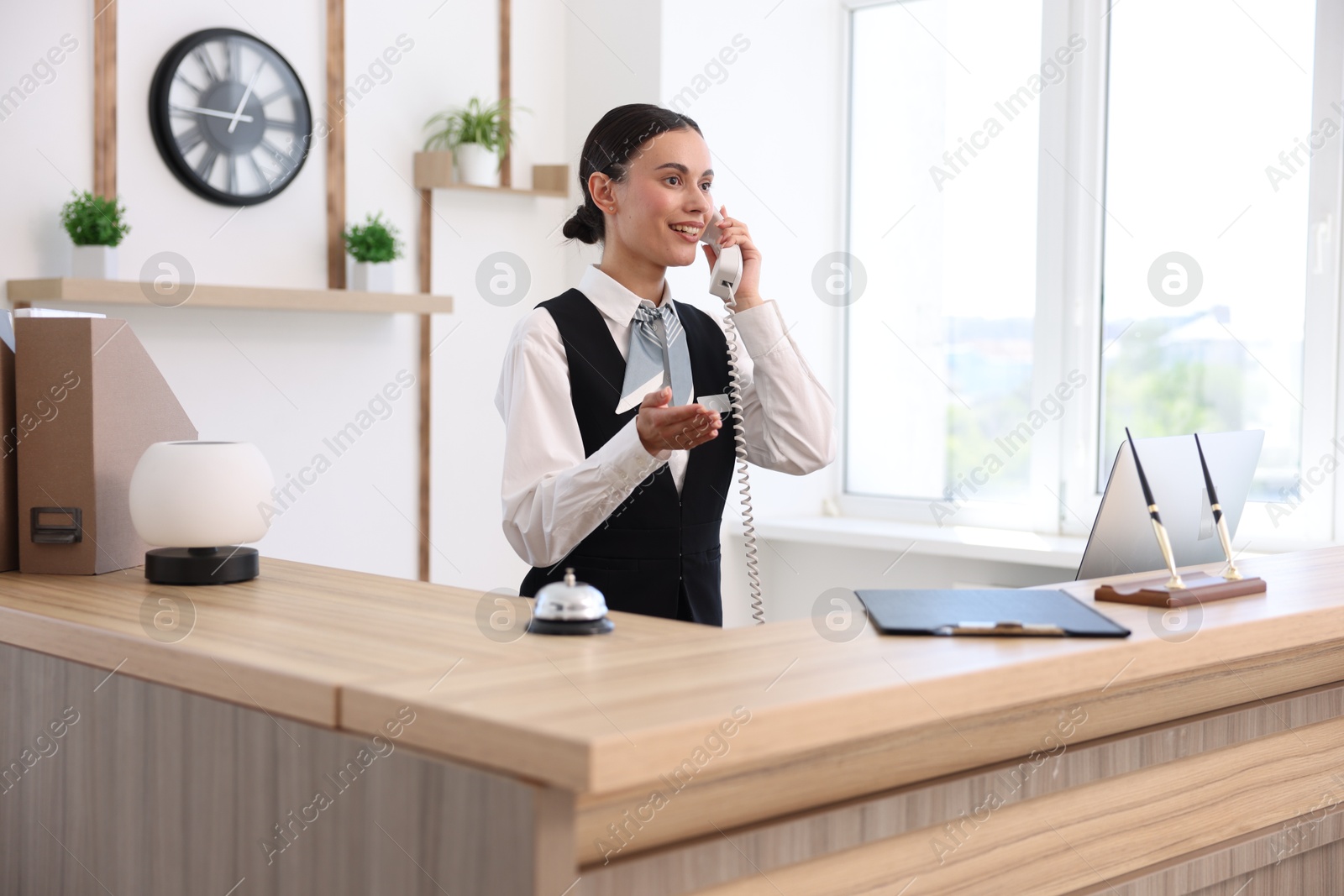 Smiling receptionist talking with client by phone at reception desk in hotel Photo of Smiling receptionist talking with client by phone at reception desk in hotel