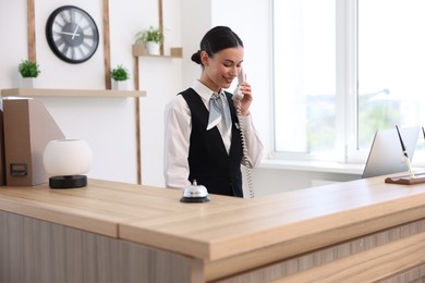 Photo of Smiling receptionist talking with client by phone at reception desk in hotel