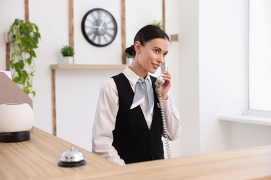 Photo of Smiling receptionist talking with client by phone at reception desk in hotel