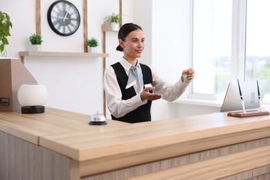 Photo of Smiling receptionist in uniform giving guest room key at reception desk in hotel