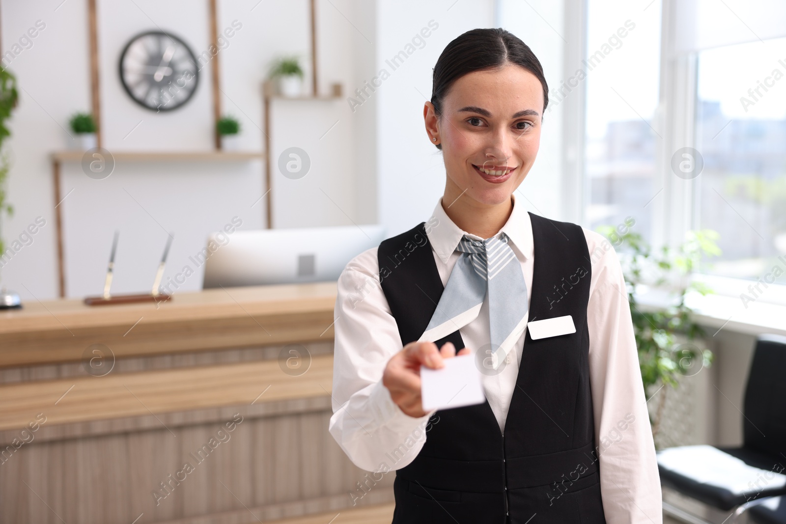 Photo of Smiling receptionist in uniform giving key card in hotel. Space for text