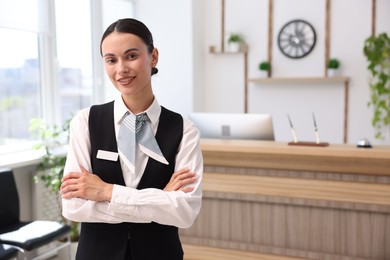 Photo of Portrait of smiling receptionist with crossed arms in hotel. Space for text