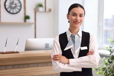 Photo of Portrait of smiling receptionist with crossed arms in hotel. Space for text